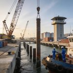 Create an editorial news illustration for an article about 'Môle Est : fin du battage des pieux, le port de Pointe-Noire se modernise'. The specific country is Republique du Congo (Brazzaville) (CG); make visual cues accurate to this exact country an